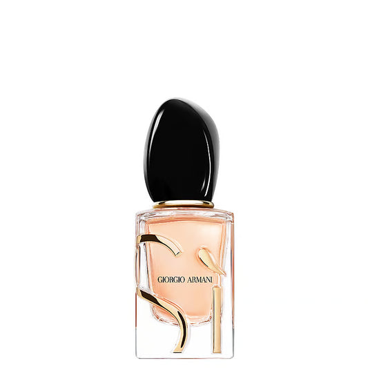 Giorgio Armani Sì Eau de Parfum – en transparent glasflaska fylld med en mjukt persikofärgad vätska. Den ikoniska "Sì"-logotypen i guld slingrar sig i 3D över glaset. Flaskan har en asymmetrisk, svart kork med en guldring runt halsen, stående mot en helt vit bakgrund.