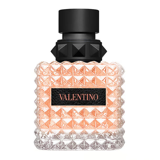 Valentino Donna Born In Roma Coral Fantasy Eau De Parfum – en kvadratisk glasflaska täckt av Valentinos ikoniska nitar. Flaskan innehåller en lysande korallfärgad vätska, och har en svart läderetikett med "VALENTINO" skrivet i korallrosa, stående mot en vit bakgrund.